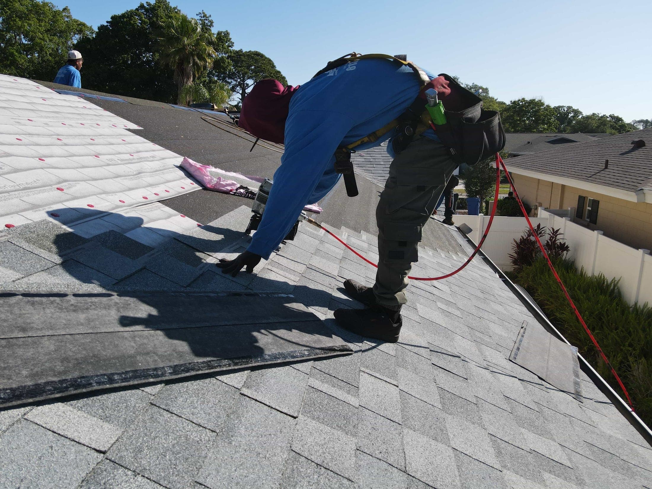 Two roofers installing shingles side by side